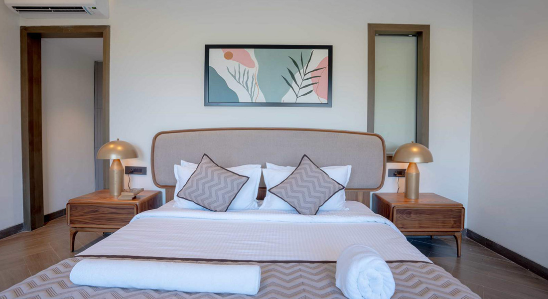 Modern villa bedroom with king-size bed, wooden side tables, table lamps, wall art, and air conditioner