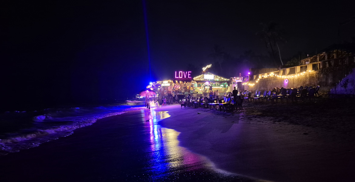 Night view of Anjuna Beach in Goa with illuminated beach shacks, sea waves, and nightlife atmosphere