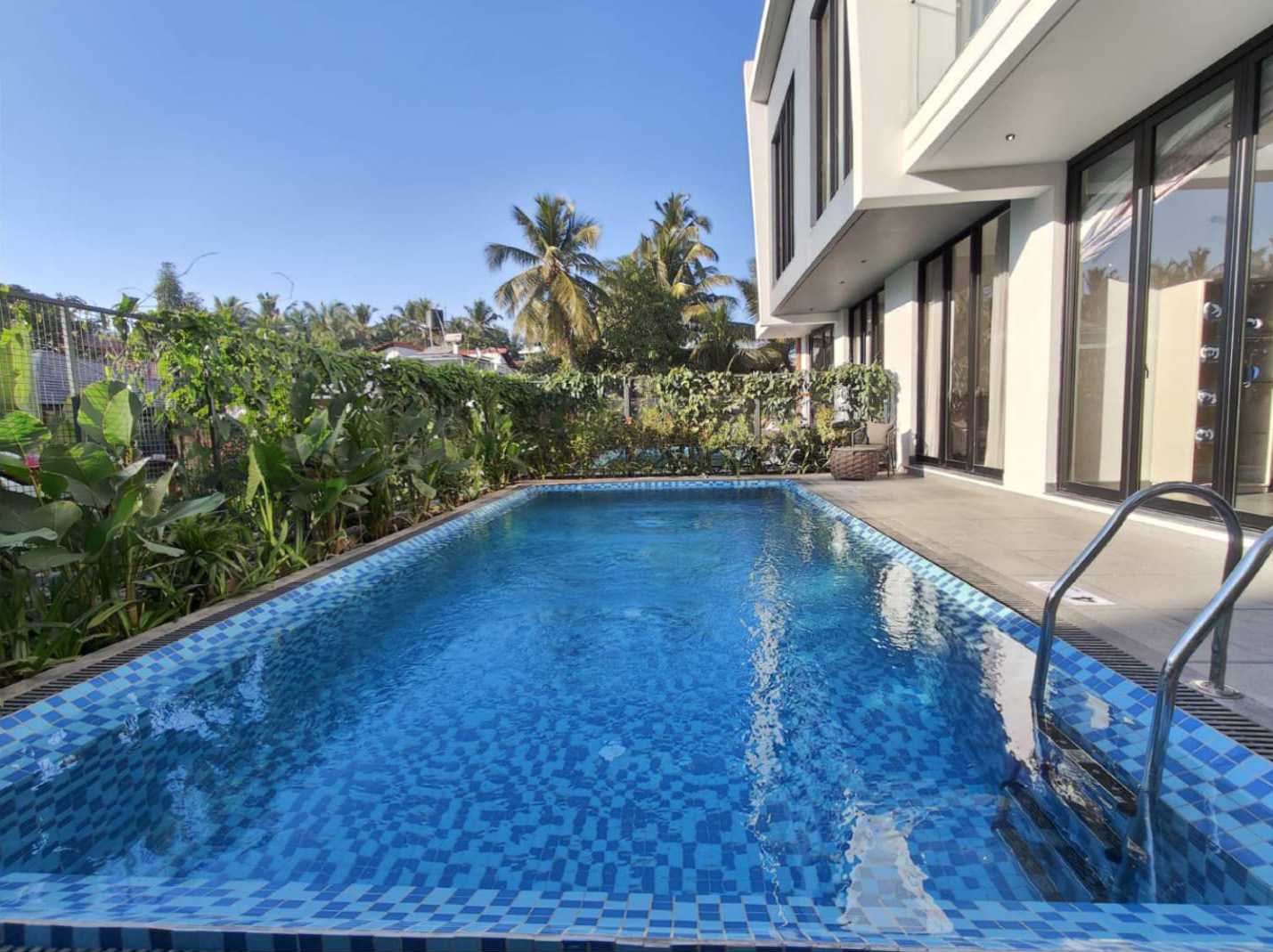 Bright blue tiled private swimming pool outside a modern white building.