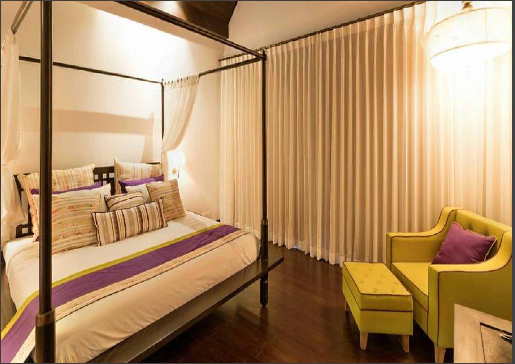 Warm bedroom with four-poster bed and yellow lounge chair