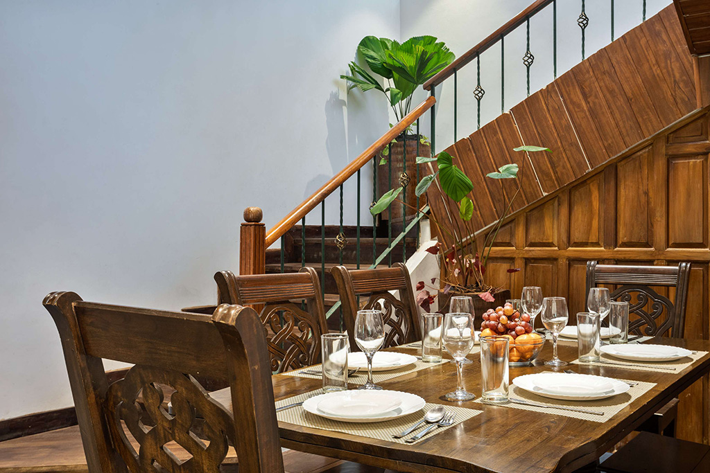 Wooden dining table set for a meal near a wooden staircase with a decorative railing