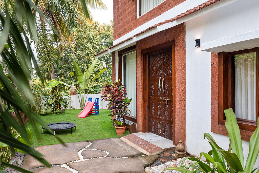Front exterior of a villa with reddish-brown stone accents and a small front yard with a trampoline and slide