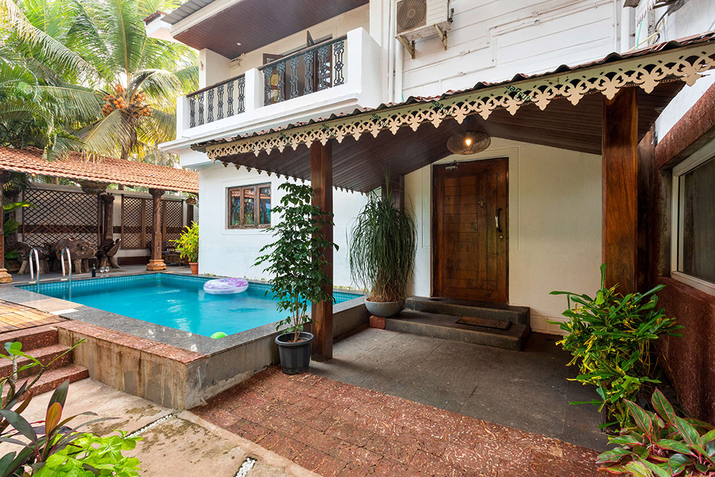 Exterior view of a white villa entrance with a small pool to the side and lush greenery