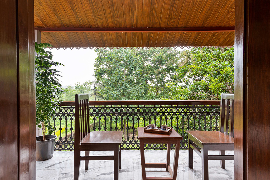 Balcony with two wooden chairs, a small table, and a view of lush trees.