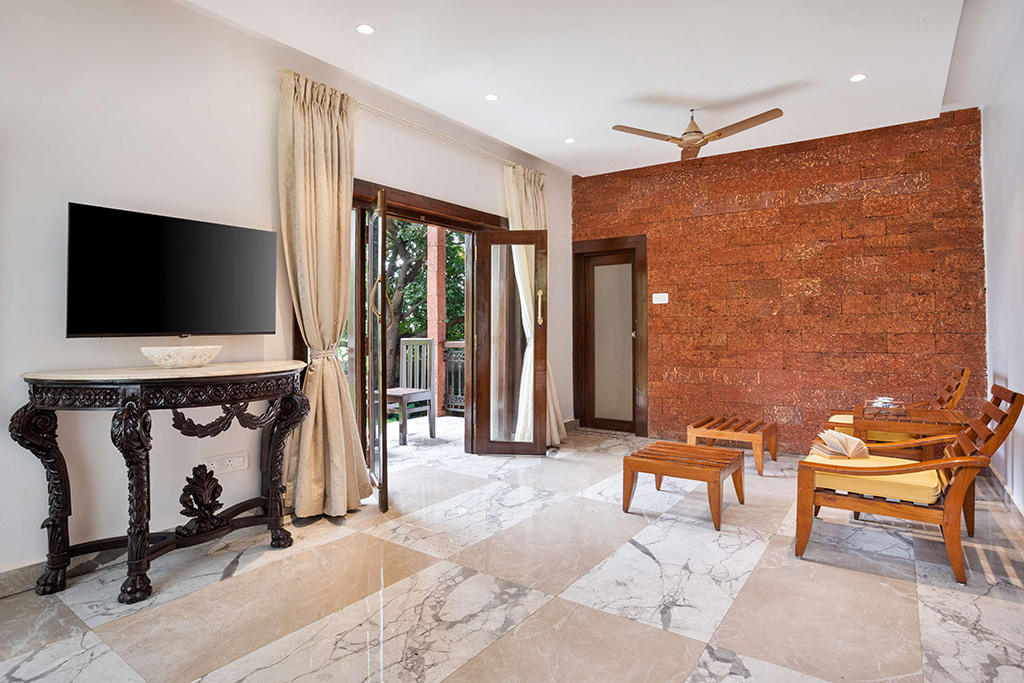 Living area with a TV on an ornate stand, a red brick accent wall, and wooden chairs