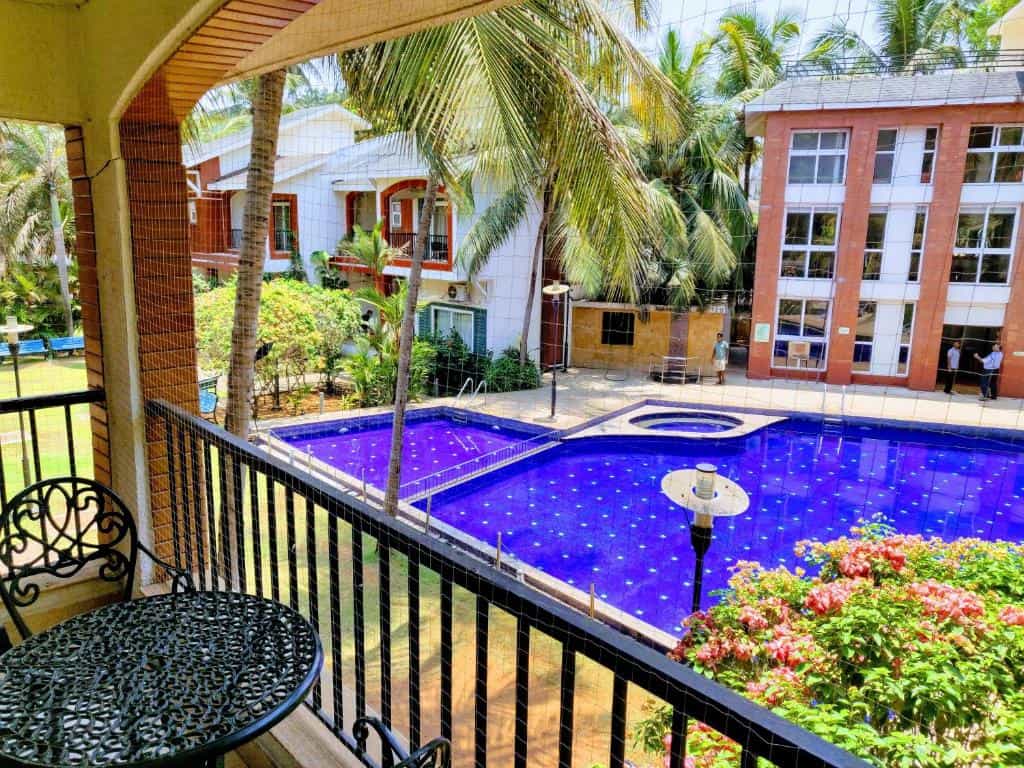 Balcony view of a villa overlooking a swimming pool with coconut trees