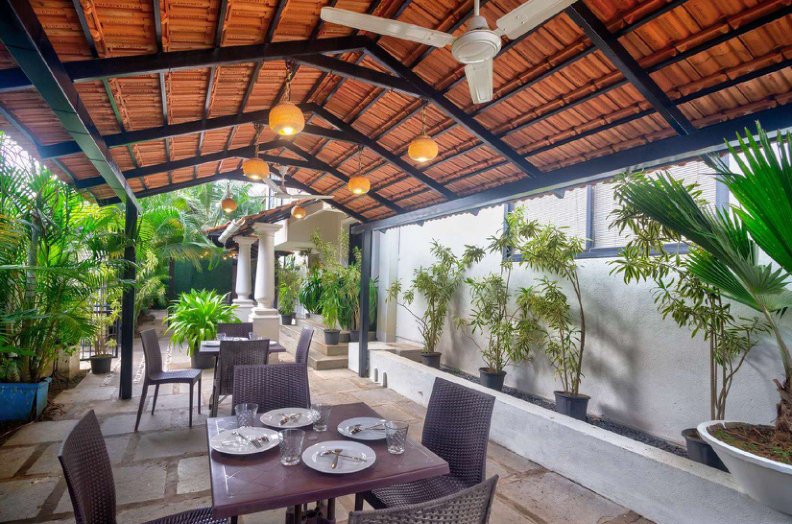 Covered outdoor dining area with wooden tables, chairs and plants