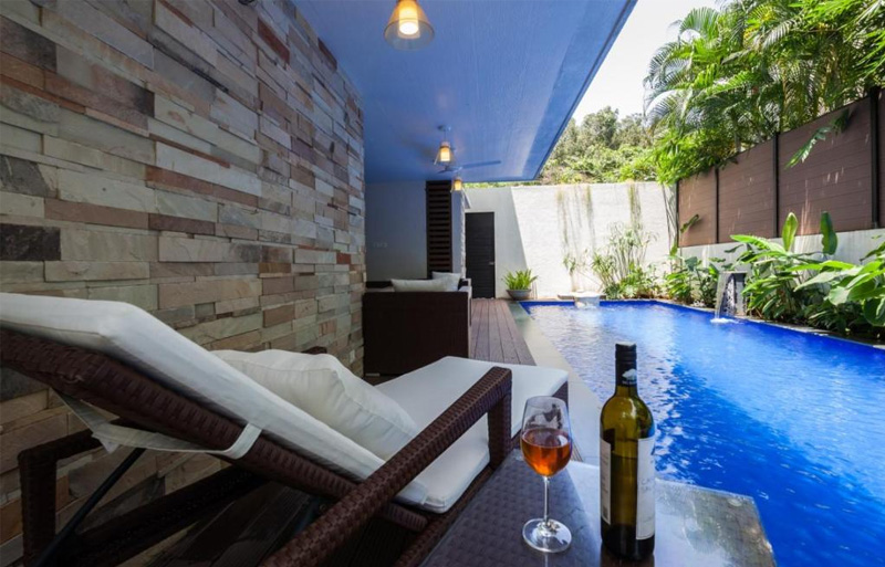 lounge chair with pool and wine bottle at Frangipani Villa in Anjuna, Goa