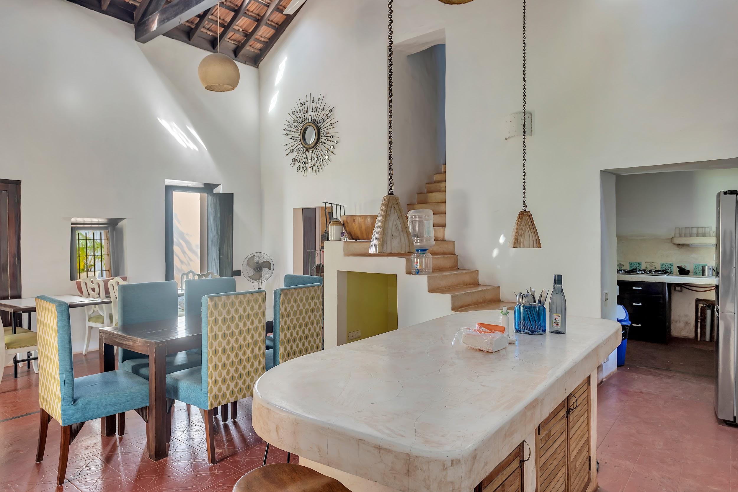 Dining area with a light counter/bar, teal upholstered chairs, and stairs leading to another level