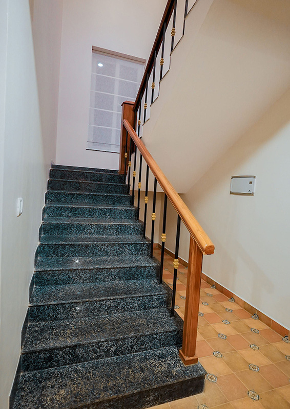 Staircase with granite steps and wooden handrail leading to upper floor