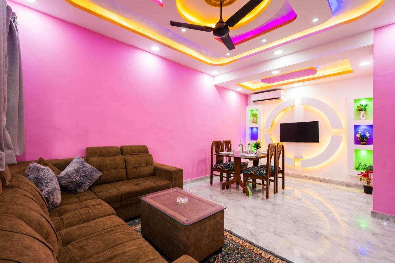 Living room with pink walls, brown sofa, dining table, and colorful ceiling lights.