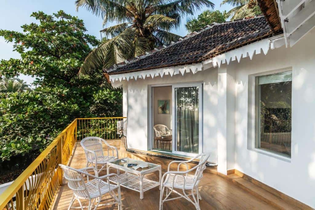 Villa balcony with outdoor seating, sliding glass doors, white wicker furniture, and tropical trees surrounding the property