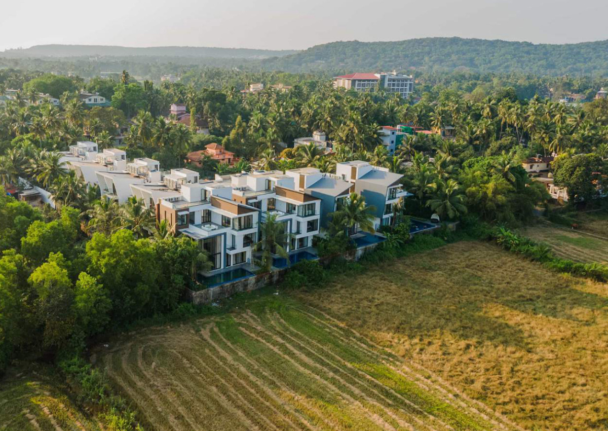 Drone view of contemporary villas bordering lush green fields and tropical landscape