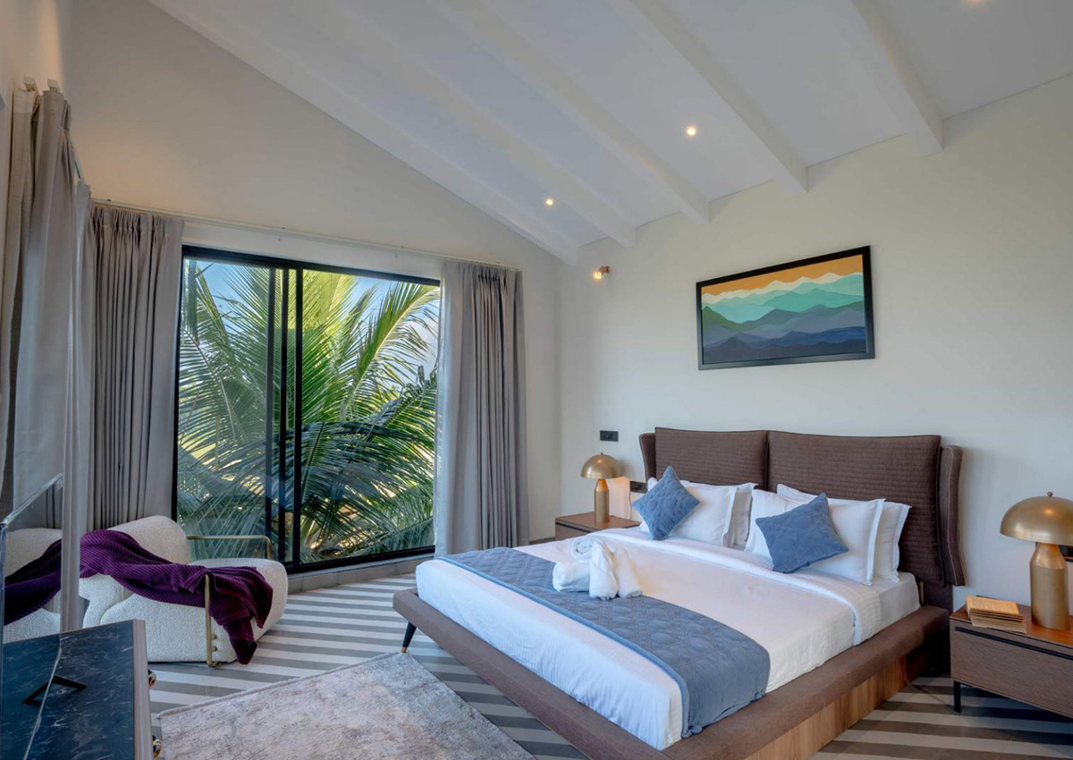 Bright bedroom with high ceiling and large window facing palm trees